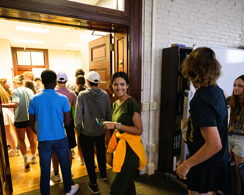 A line of high school students entering a room. One student in the middle of the photo turns and smiles at the camera.