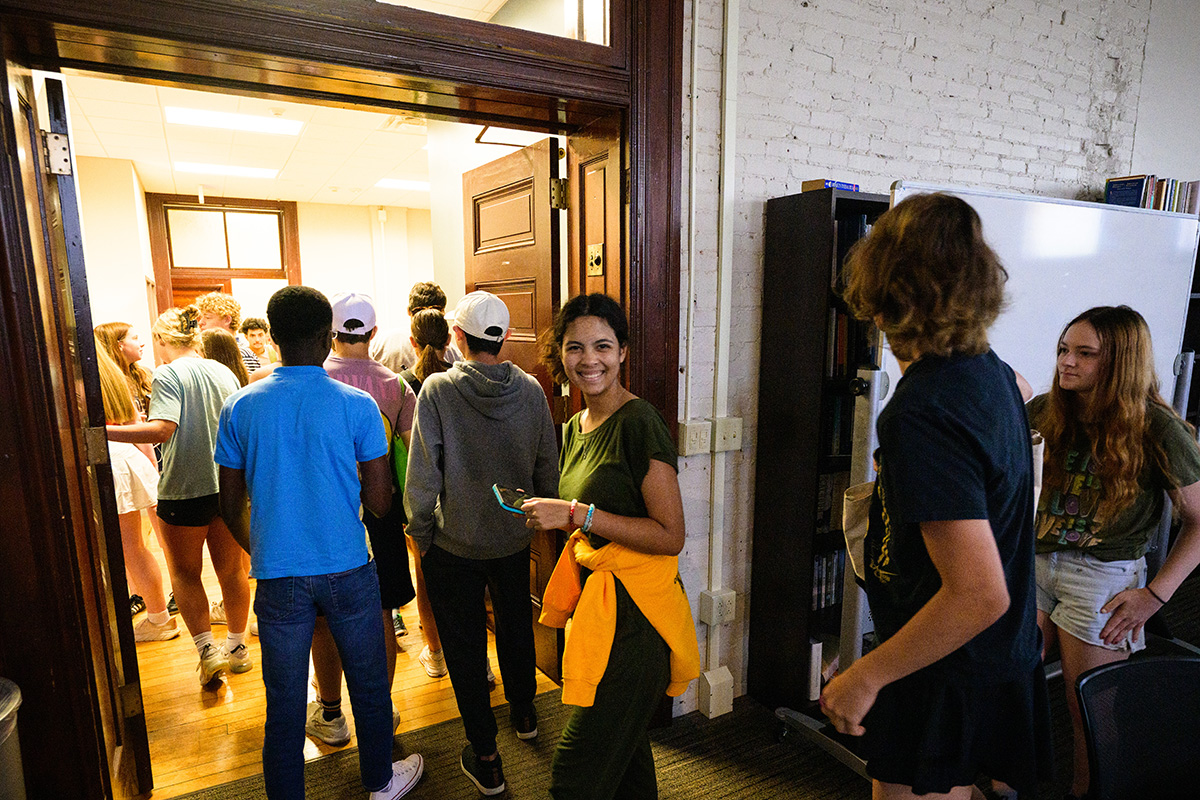 A line of high school students entering a room. One student in the middle of the photo turns and smiles at the camera.