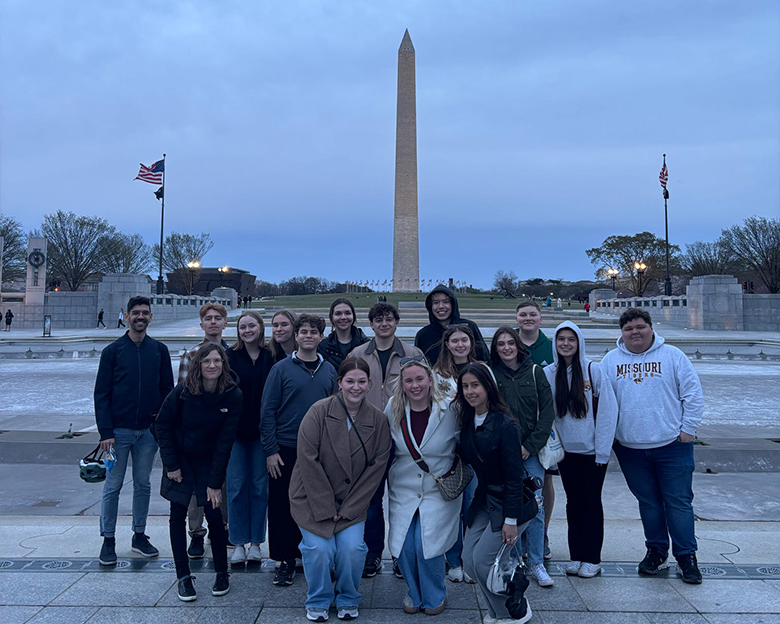 A group of students stand together and smile in front of the Washington monument.