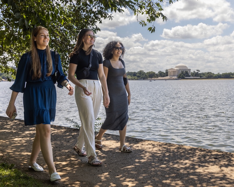 Three women walk along the Potomac River, the Lincoln Memorial in the background.