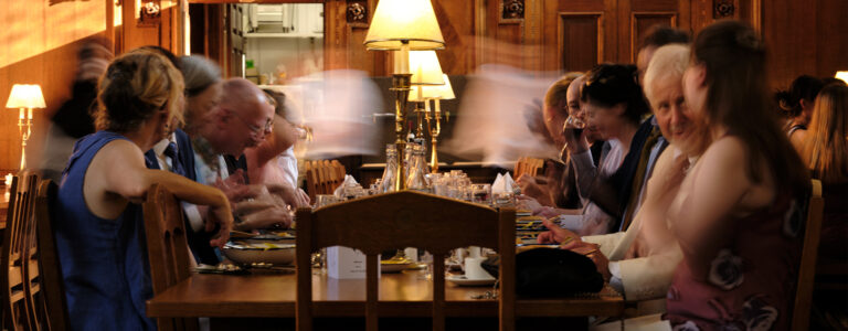 A group of people sit across from each other and eat a meal at a long table.