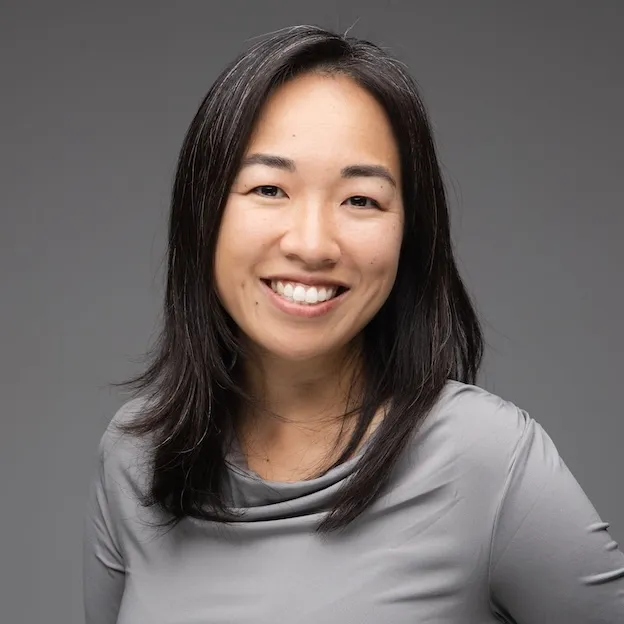 A professor with black hair and a gray shirt smiles for the camera