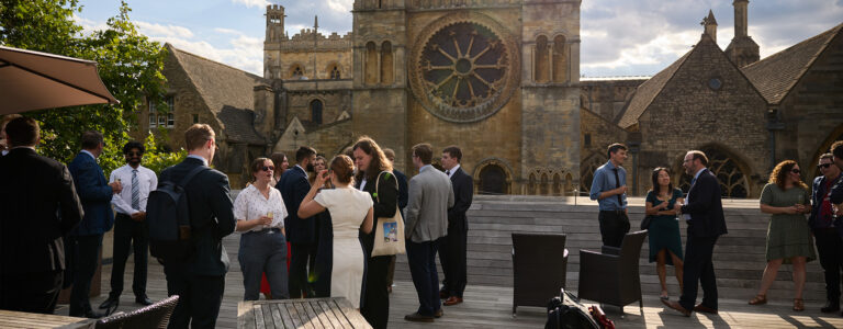 People in nice clothes chat in groups on an outdoor patio at Oxford.