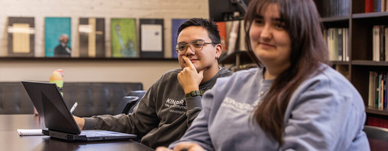 Two students sit at a table and look at someone off camera.