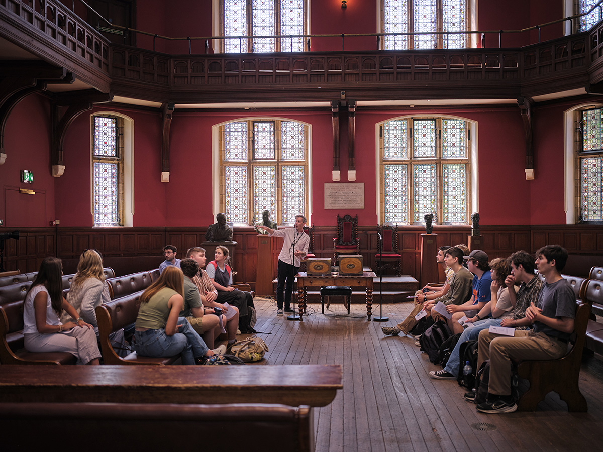 A group of students sits in a room at Oxford University and listens to a speaker.
