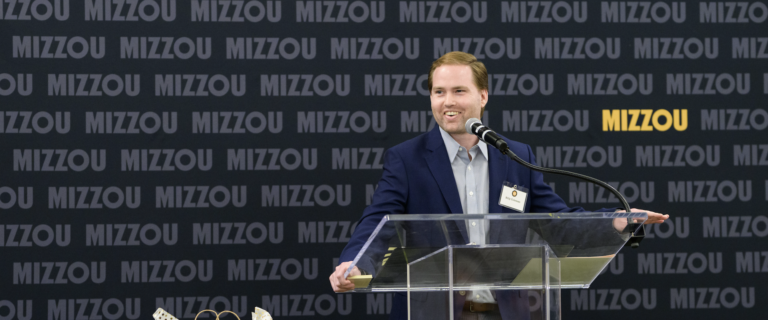 A man in a suit speaks happily from a clear podium.