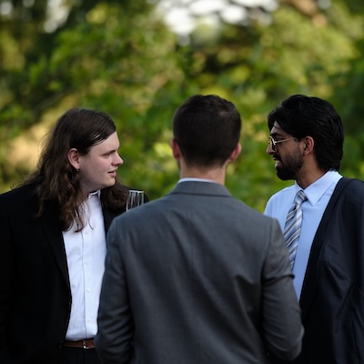 Three men engaged in conversation on a veranda.