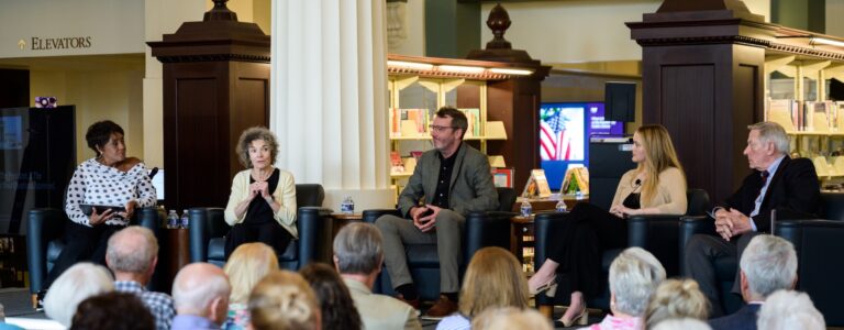 A panel of five scholars speaks in front of an audience at the Kansas City Public Library.