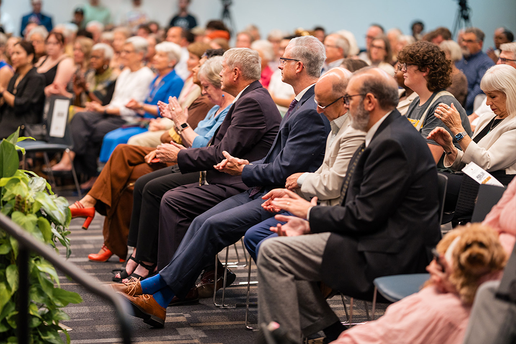 Audience members applaud an off-camera speaker.