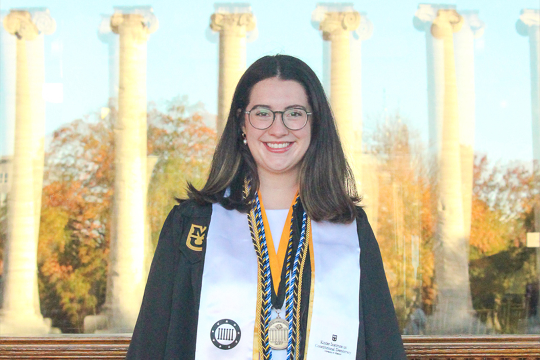 A Kinder Institute graduate wears graduation regalia and smiles.
