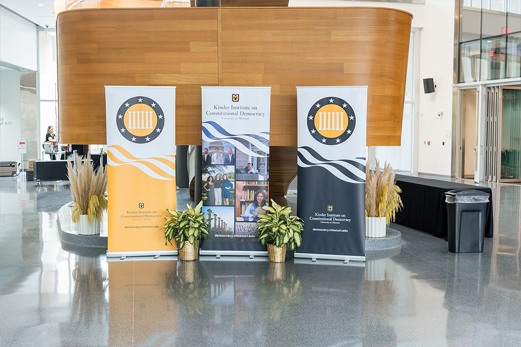 Large vertical banners with photos and the Kinder Institute logo are set up in a building lobby.