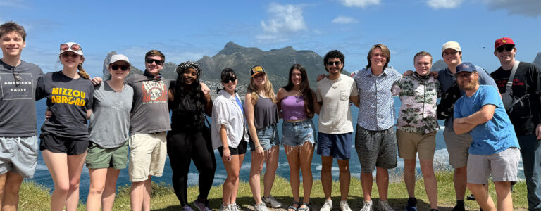 A group of students stand together and smile in front of the ocean.