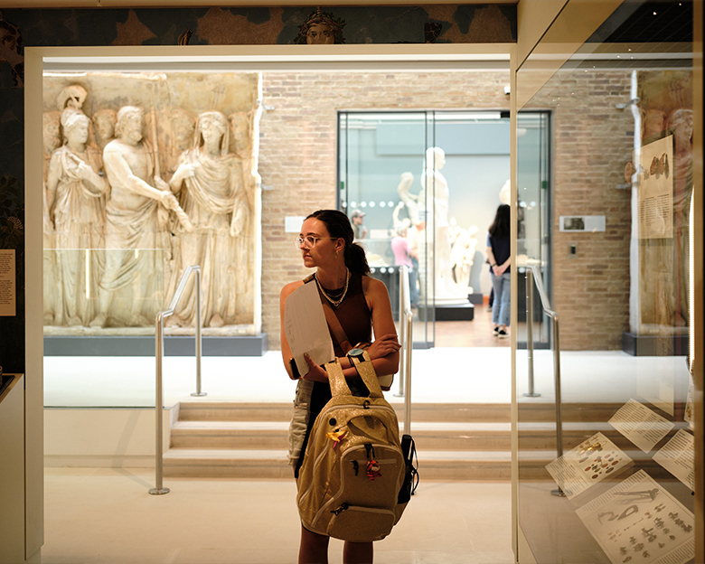 A student looks at exhibits in a museum. There are sculptures in the background.