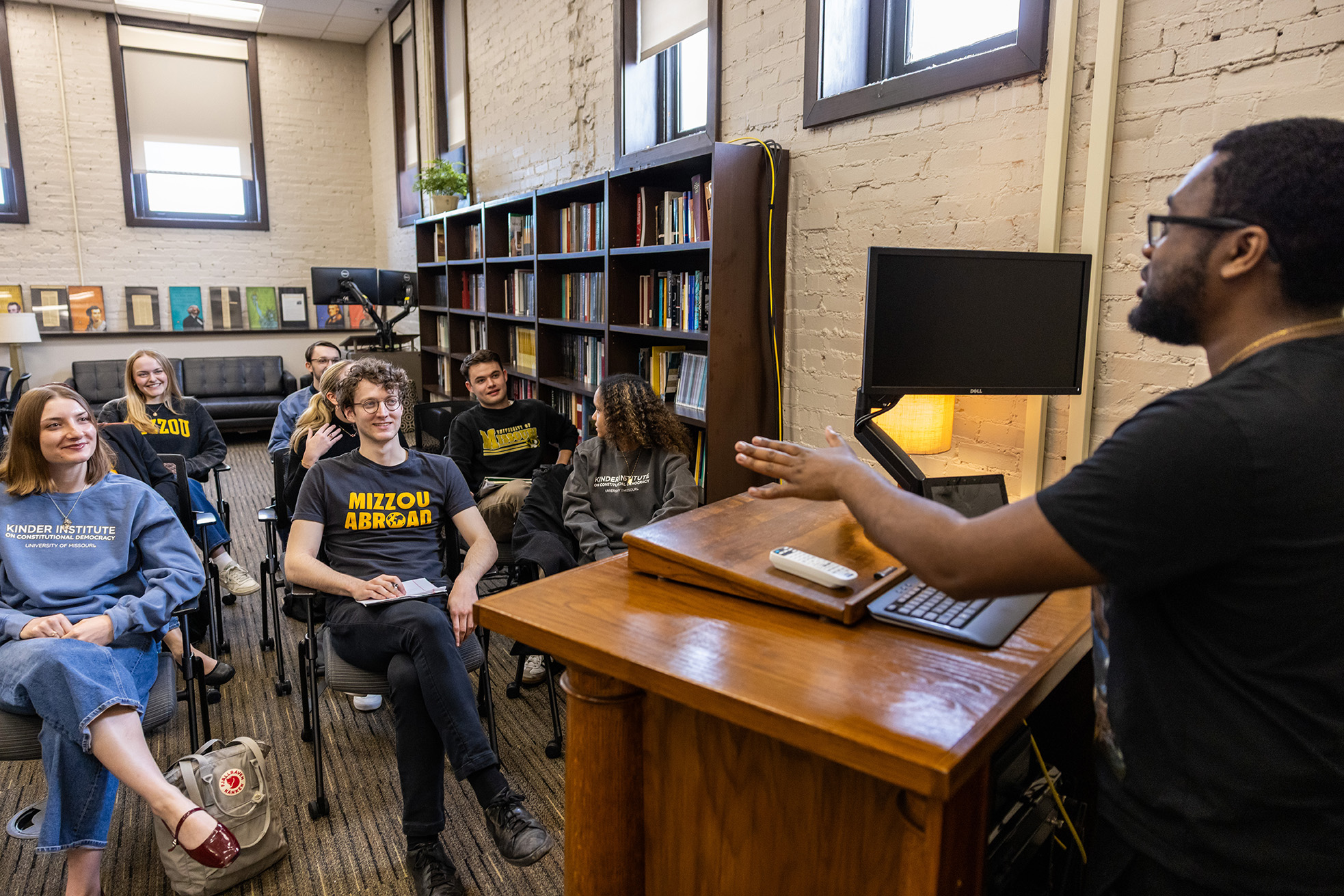 A student speaks at a podium while other students sit and listen.