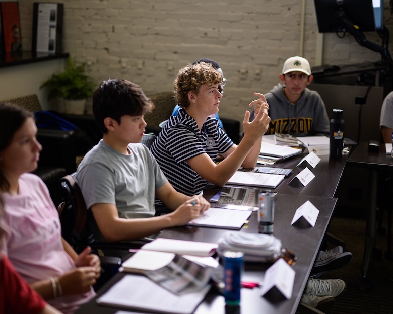 A student at a conference gesticulates with his hands while making a point.