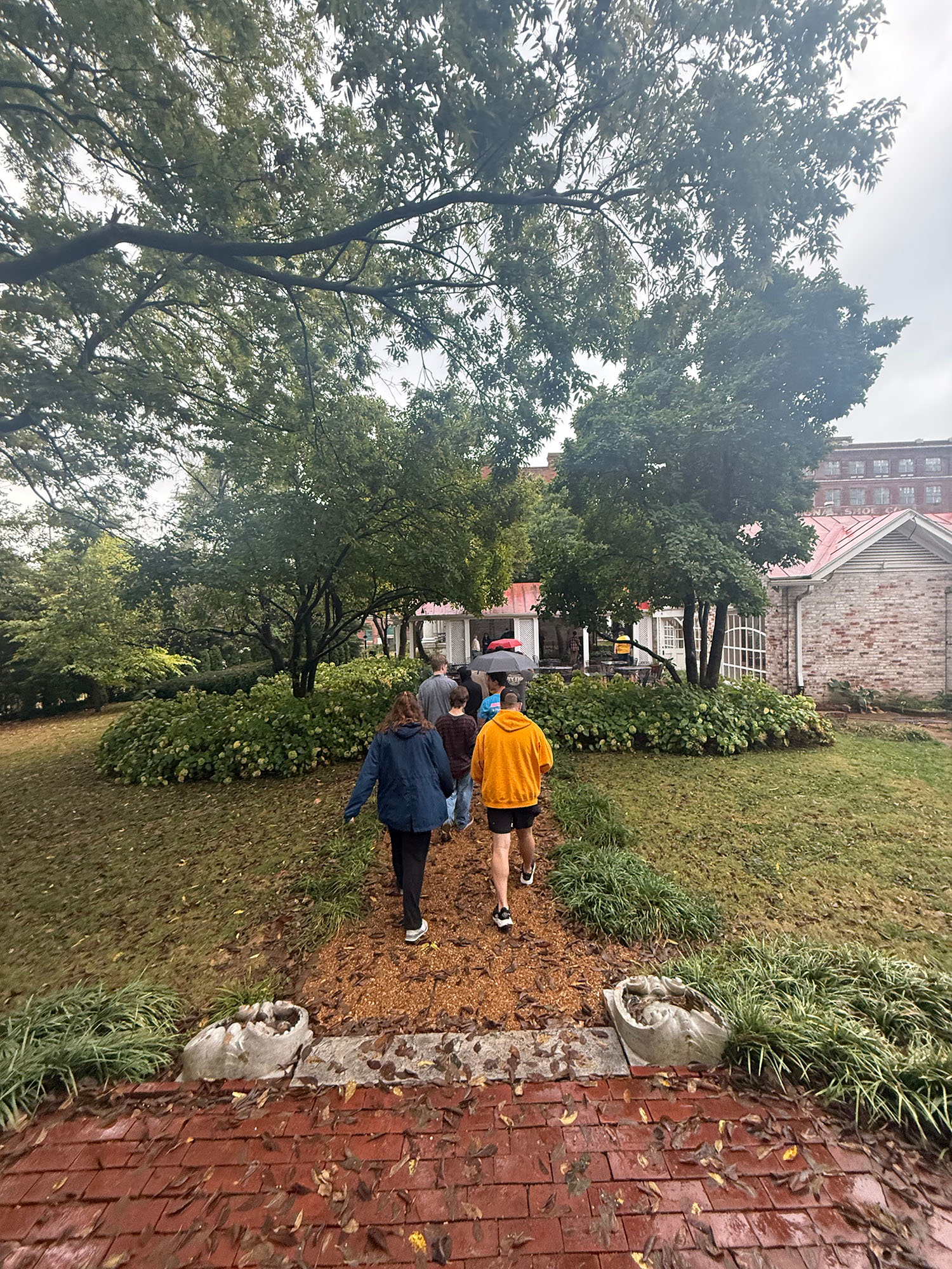 A group of students walk down a garden path under trees.