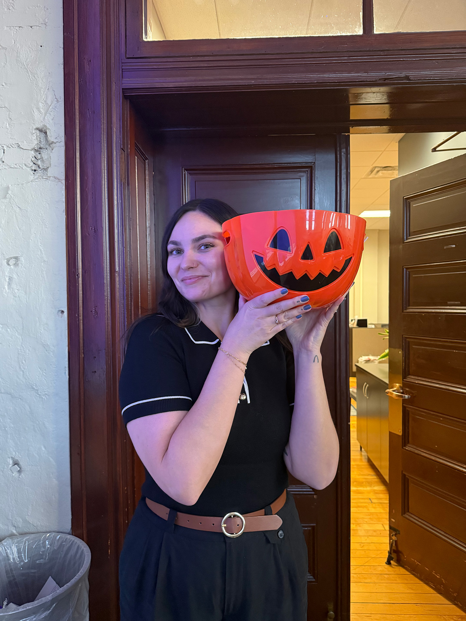 A student smiles and holds up a plastic pumpkin Halloween bucket.