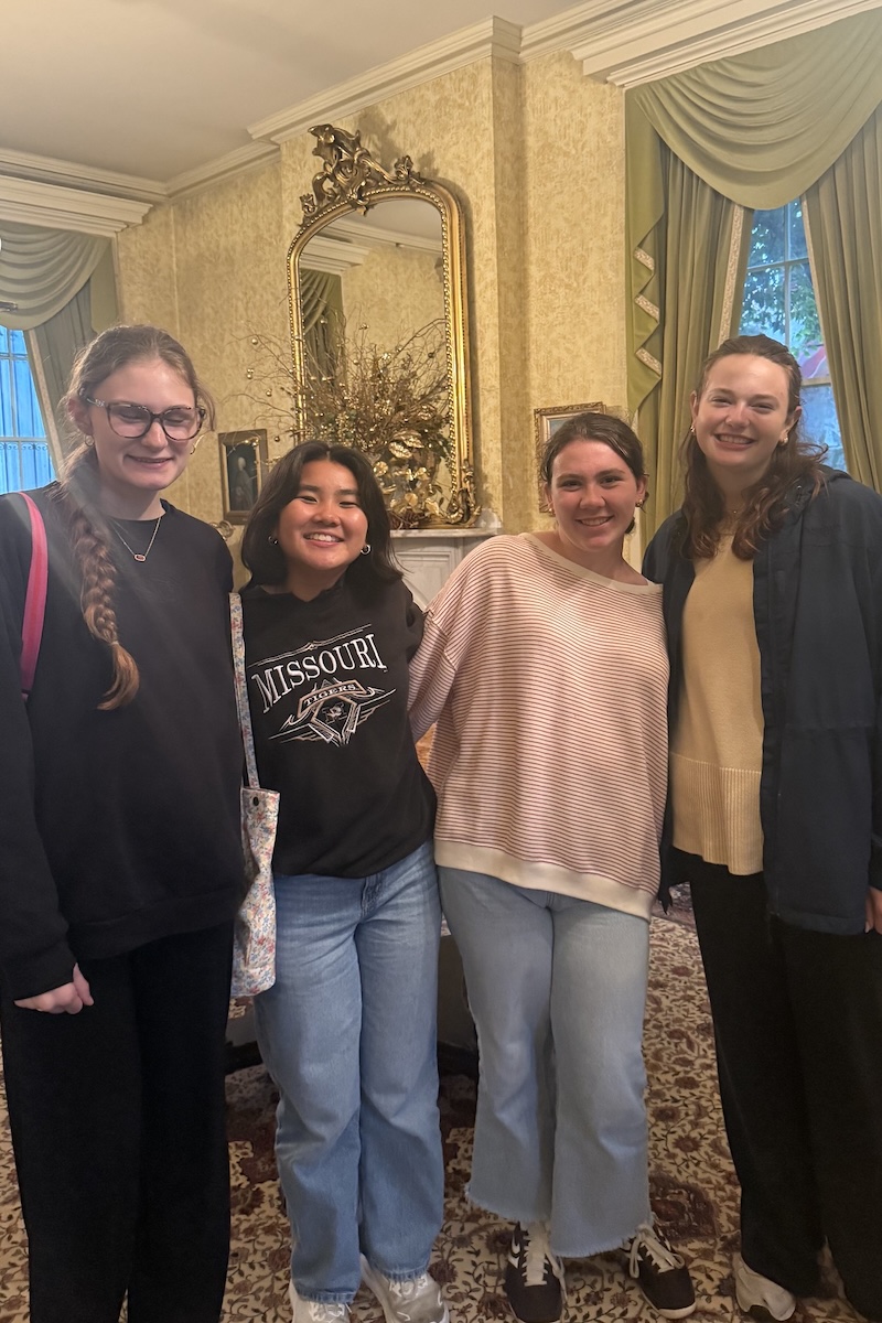 Four college students smiling, their arms around one another, at a St. Louis museum