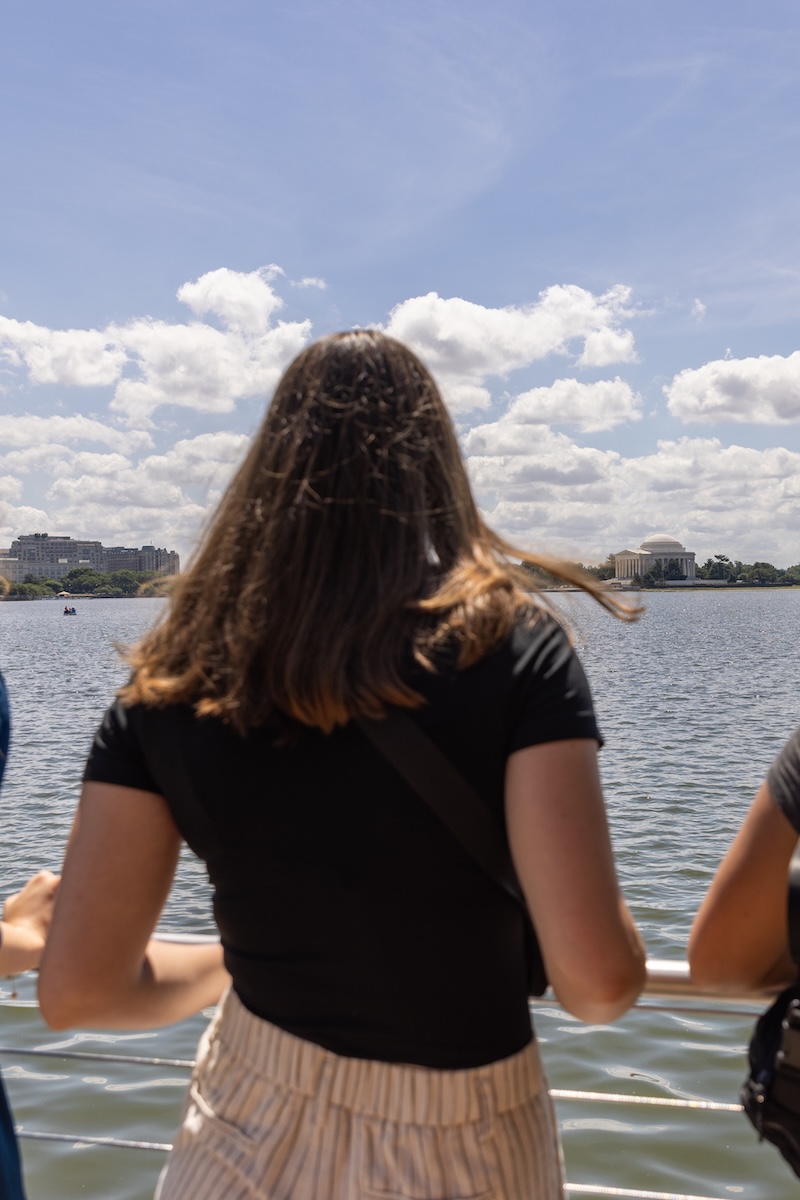 A college student, back turned to the camera, gazes over the Potomac River, the Washington Monument in the distance.