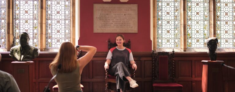 A student being photographed sitting in a medieval throne