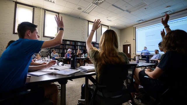 Students raise their hands to answer a professor's question.