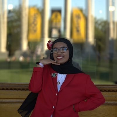A student poses in front of Mizzou's Jesse Hall, the reflections of historic columns in the window behind her.