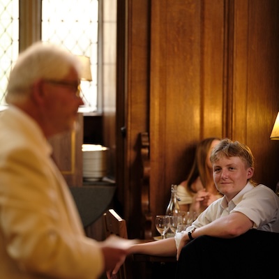 A student smiles as he listens to a dinner speaker in an Oxford dining hall.