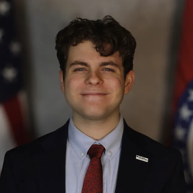 A young man in a suit poses between the US and Missouri State flags
