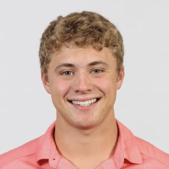 A young man in a salmon colored polo-style shirt poses for a headshot