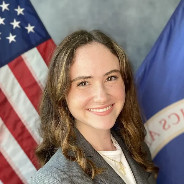 A young woman with brown hair poses for a headshot in front of the US and NASA flags.