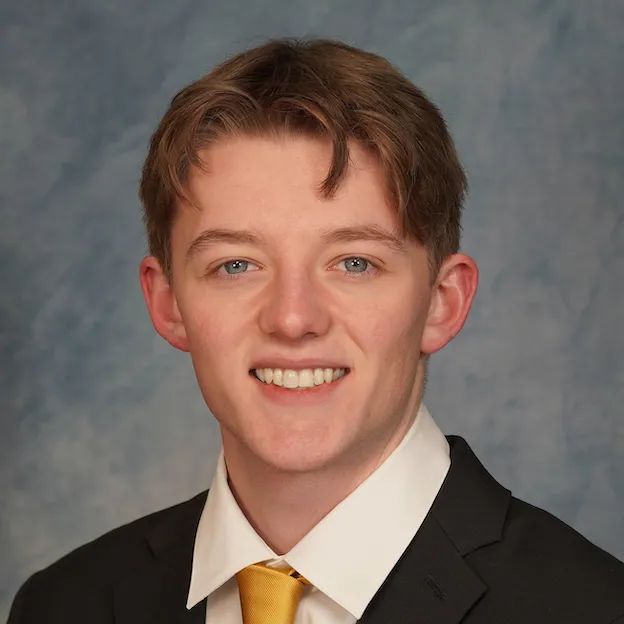 A young man in a suit and tie poses for a headshot in front of a gray backdrop