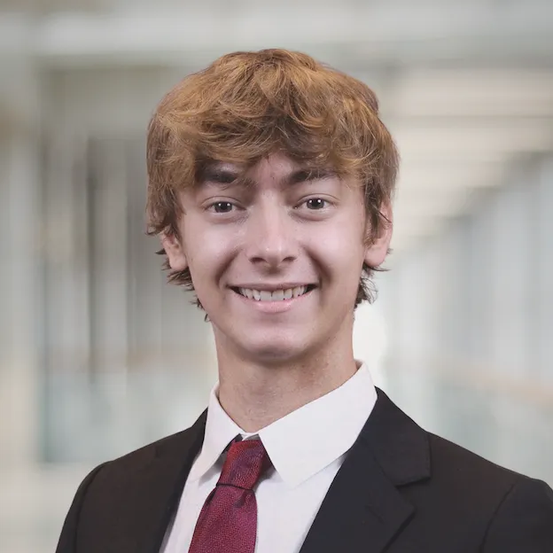 A young man in a suit poses for a headshot in a hallway, blurred for effect