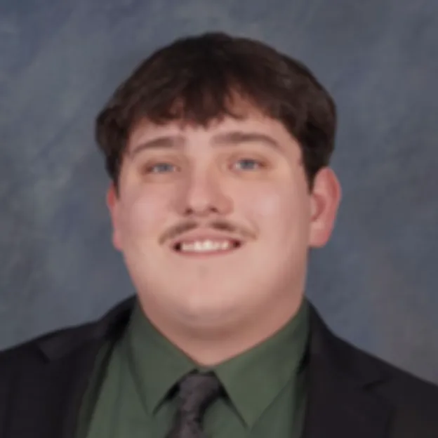 A young man with a mustache and wearing a suit poses for a professional headshot