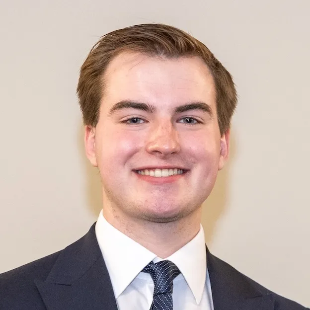 A young man in suit and tie poses for a professional headshot in front of a beige background
