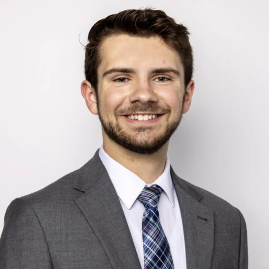 A young, bearded man in a suit and tie poses for a professional headshot