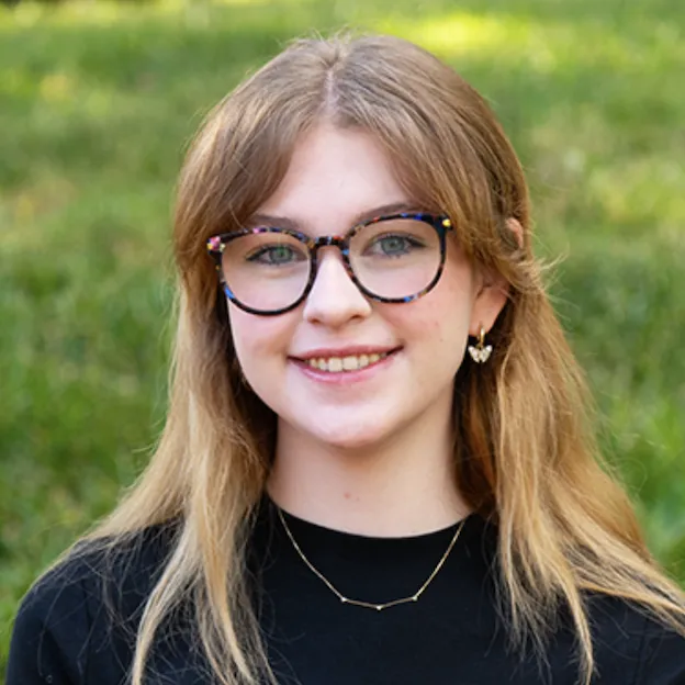 A young woman with glasses smiles in a verdant field of grass