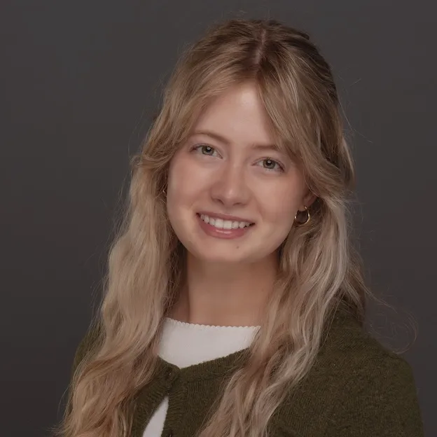 A young woman with blonde hair poses for a professional headshot in front of a deep gray backdrop