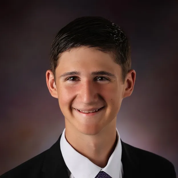 A young man in a suit and tie poses for a professional headshot in front of an iridescent backdrop