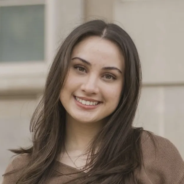 A young woman with brown hair smiles in front of a university building
