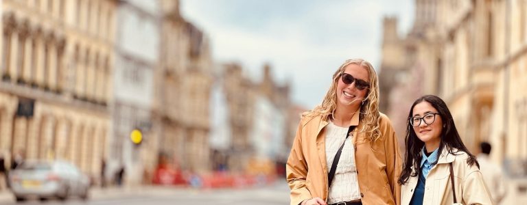 Two college age women stand on the sidewalk in Oxford