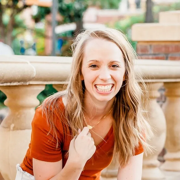 A woman, smiling, sits on a veranda